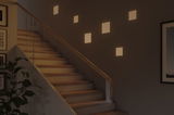 Modern staircase with wooden steps and glass railing lit by warm white square wall lights