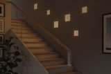 Modern staircase with wooden steps and glass railing lit by warm white square wall lights
