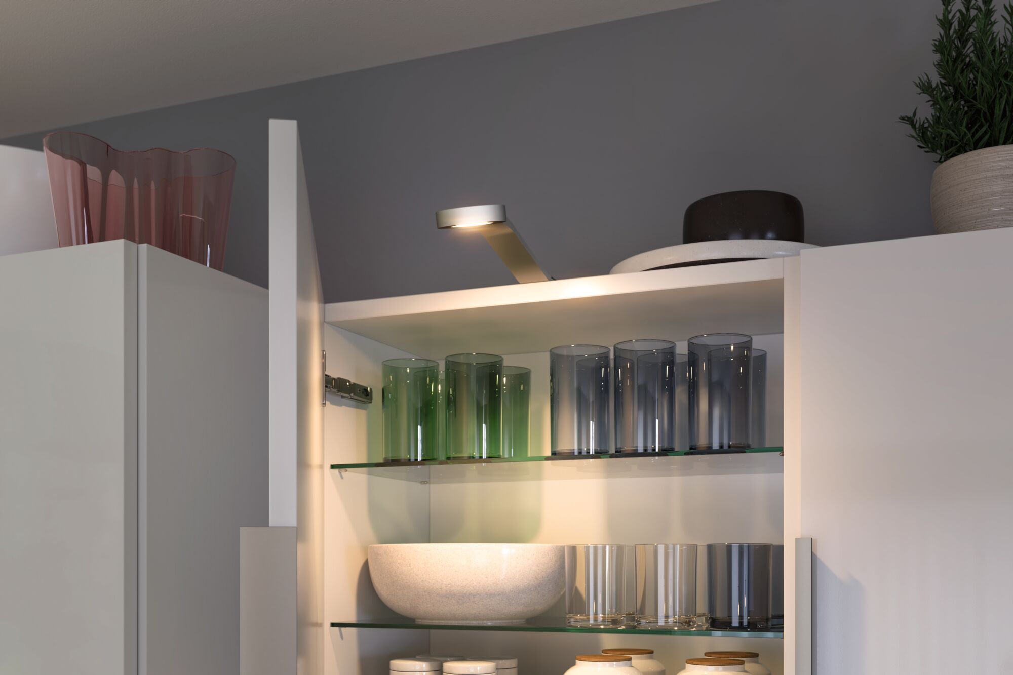 Weiße Küchenschrankbeleuchtung mit LED-Lampe über Glasregalen mit bunten Trinkgläsern und Schalen.