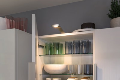 Witte keukenkast LED-verlichting boven glazen planken met gekleurde drinkglazen en kommen.