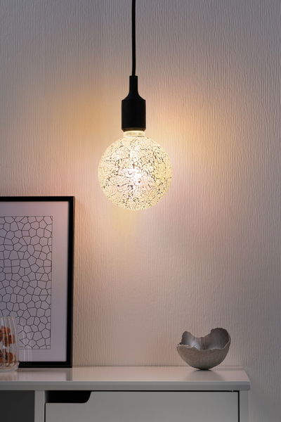 Hanging light bulb with white mosaic glass surface and black cable above white desk.