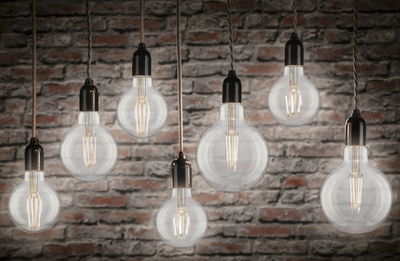 Seven mixed filament globe bulbs with black sockets hanging against stone wall in 4000K warm white light