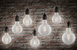 Seven mixed filament globe bulbs with black sockets hanging against stone wall in 4000K warm white light