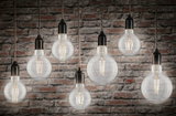 Seven mixed filament globe bulbs with black sockets hanging against stone wall in 4000K warm white light