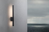 Schwarze LED-Wandleuchte aus Metall mit indirektem Licht an grauer Außenwand mit Meerblick