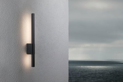 Black metal LED wall light with indirect illumination on grey exterior wall by the sea