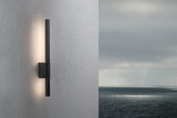 Black metal LED wall light with indirect illumination on grey exterior wall by the sea