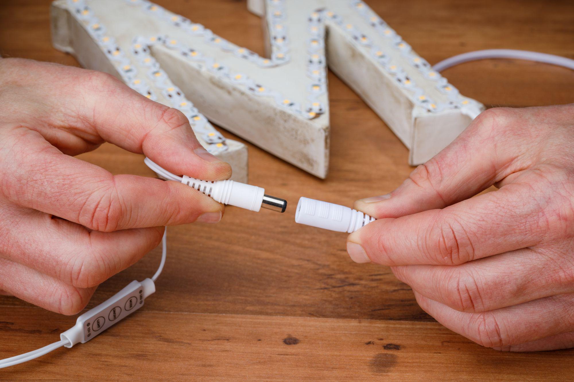 Handen verbinden witte LED-stekker met bedradingskabel op houten ondergrond met LED-letter.