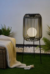 Zwarte metalen vloerlamp met ronde witte lamp in tuin op groen gras naast deken en planten