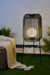 Black metal floor lamp with round white light in garden on green grass near blanket and plants