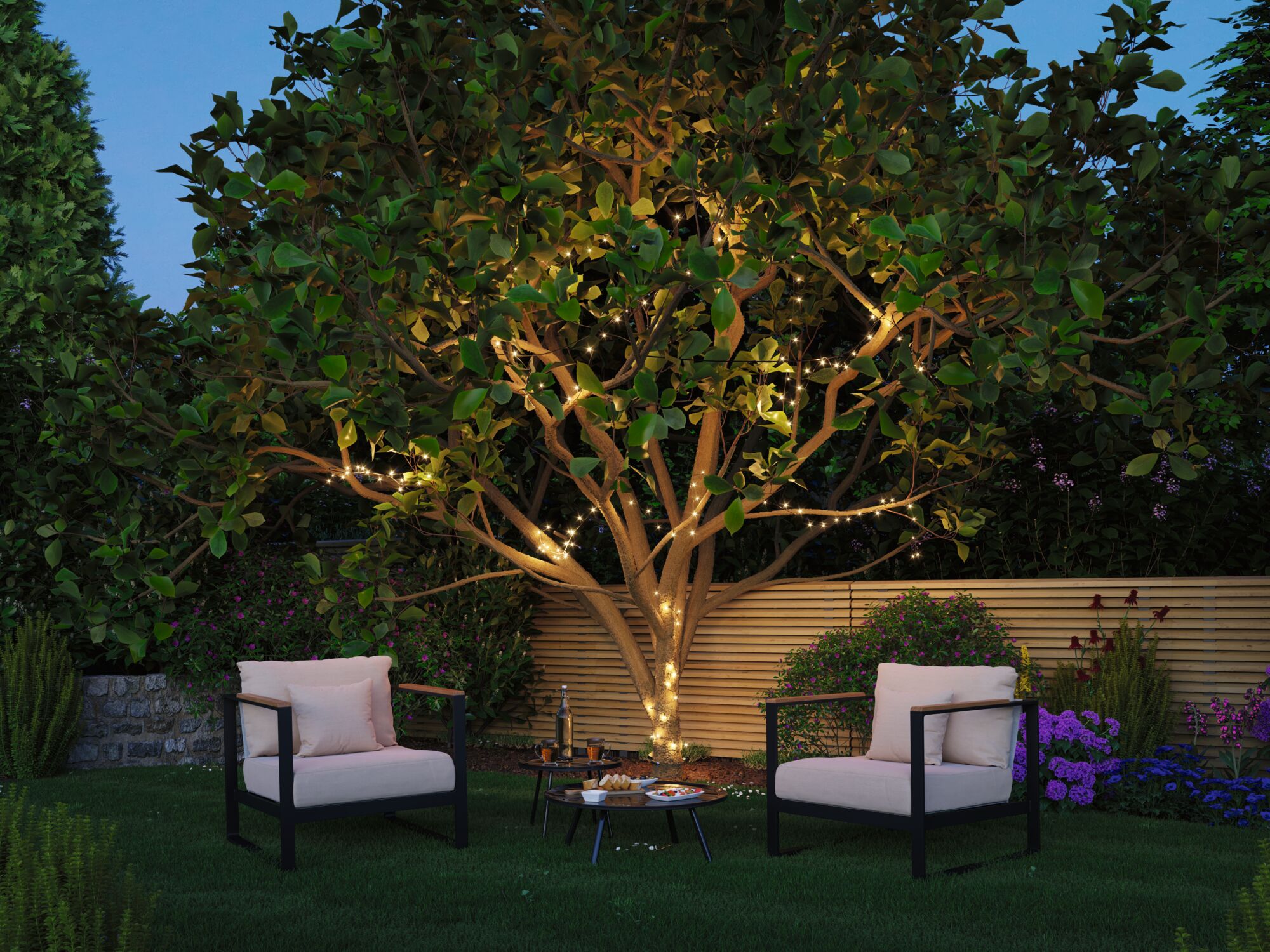 Garten mit Baum, der mit warmweißen LED-Lichterketten beleuchtet ist, umgeben von Sitzmöbeln und Pflanzen
