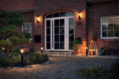 Illuminated house entrance with white doors, red brick walls, and modern black outdoor lights for garden and patio.