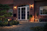 Beleuchteter Hauseingang mit weißen Türen, roten Ziegelwänden und modernen schwarzen Außenleuchten für Garten und Terrasse.