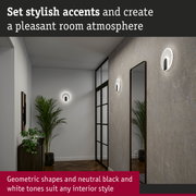 Modern round white and black LED wall lights on grey wall with mirror and plants in hallway interior