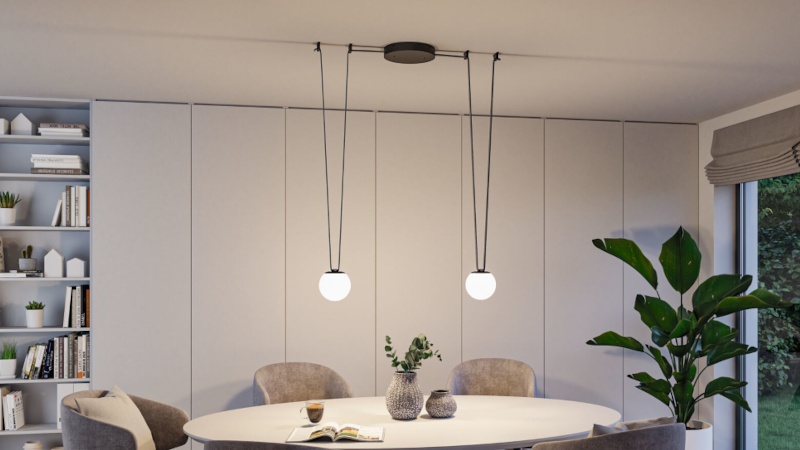 Moderne hanglamp met twee witte bollen en zwarte snoeren boven ronde eettafel in lichte kamer