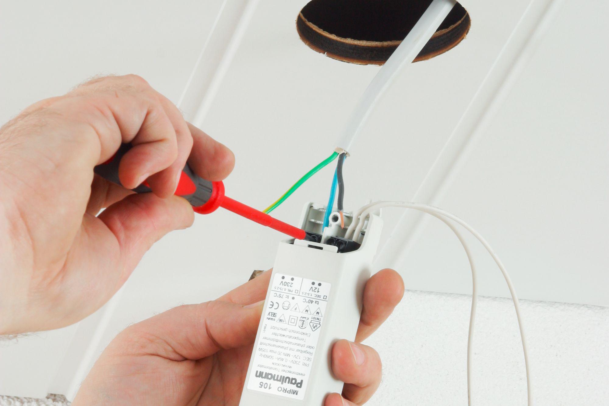 Hand connecting white cables to Paulmann Mipro 105 LED lighting transformer using screwdriver.