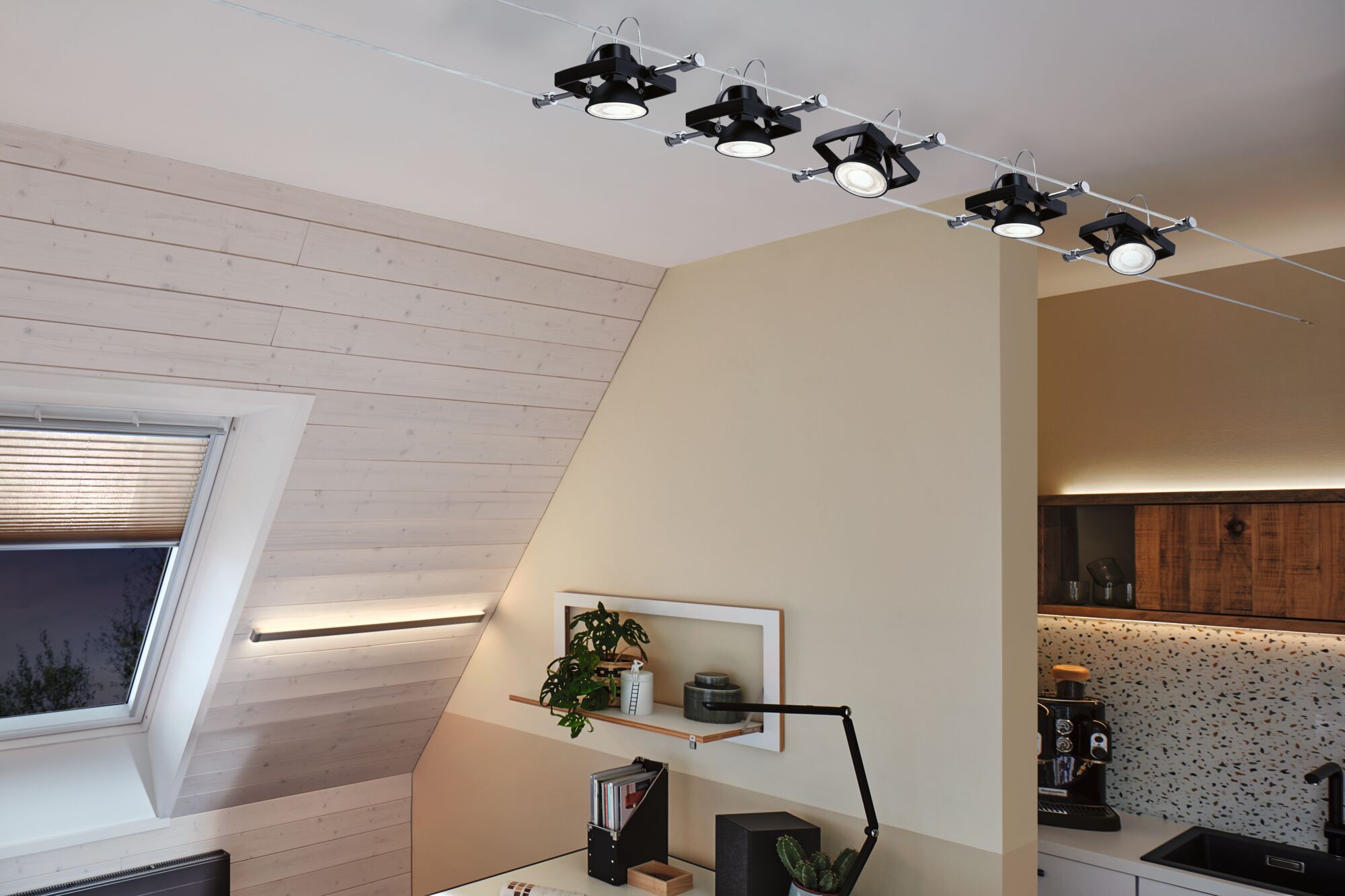 Black LED cable spotlights with adjustable heads on white ceiling in modern living space with wood paneling.