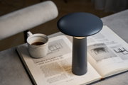 Black metal LED table lamp on open book beside marble coffee cup for cozy reading light