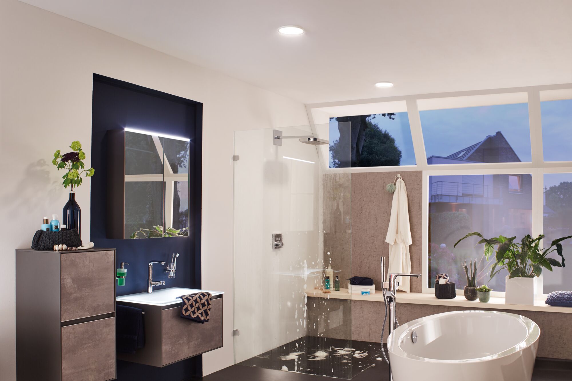 Modern bathroom with freestanding bathtub, glass shower, and grey wood-effect cabinets.