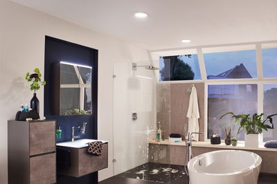 Modern bathroom with freestanding bathtub, glass shower, and grey wood-effect cabinets.