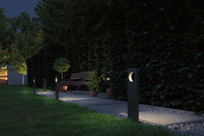 Lampes de jardin noires en métal modernes éclairent un chemin avec banc et plantes la nuit