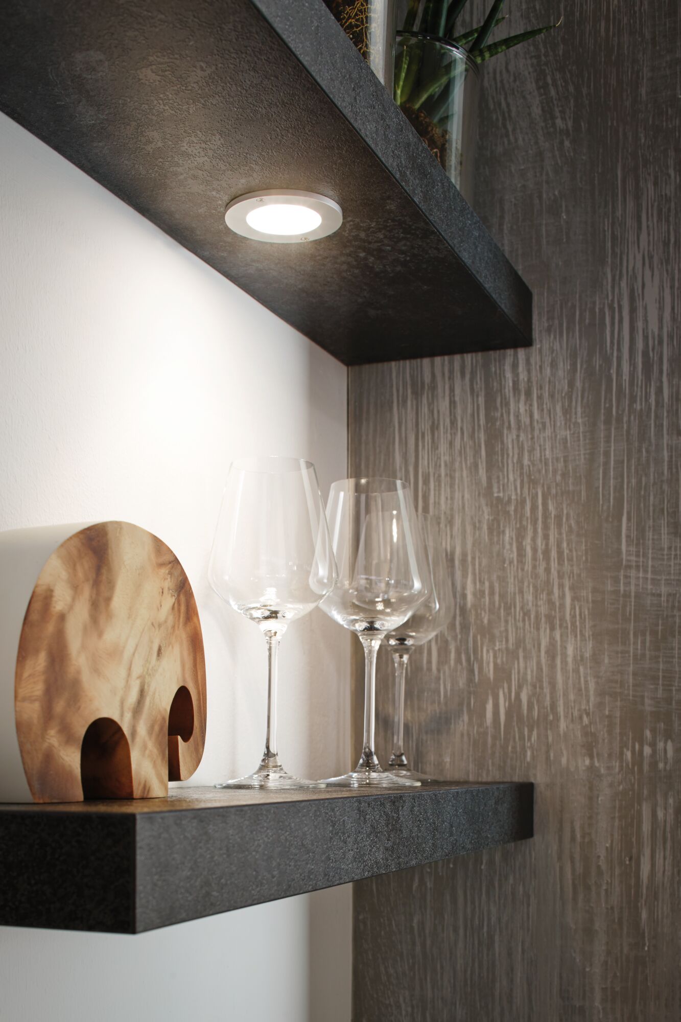 Rundes LED-Unterbauleuchte in Weiß an schwarzem Regal mit Weingläsern und Holzdeko in moderner Küche