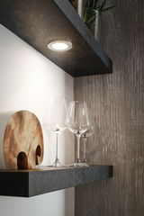 Lumière LED ronde blanche sous meuble sur étagère noire avec verres à vin et décoration en bois dans cuisine moderne