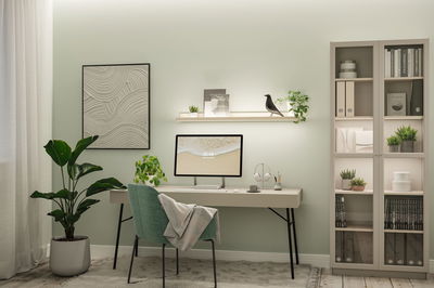 Modernes Home-Office mit hellem Schreibtisch, grünem Stoffstuhl und dekorativer Wandbeleuchtung von Paulmann.