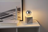 Moderne tafellamp met geometrische betonnen voet en halfzilver bolvormige lamp in grijs en zilver.