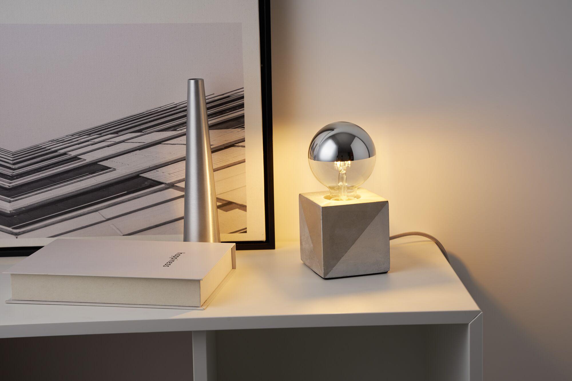 Moderne bordlampe med geometrisk betonfod og halvsølvet pære i grå og sølvfarver.
