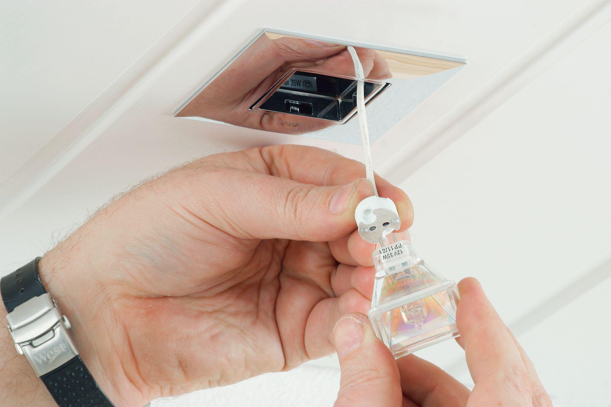 Hand installing square recessed light with clear 12V 35W halogen bulb in white ceiling