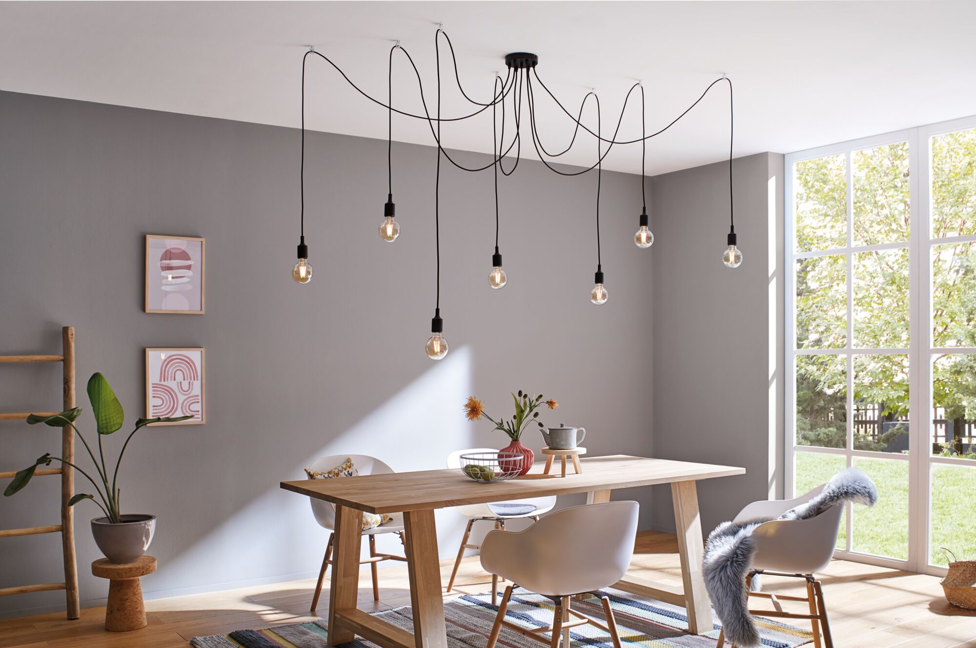 Moderne eetkamer met lichte houten tafel, witte stoelen en zwarte hanglamp met gloeilampen.