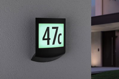 Black LED house number sign with illuminated white-green panel showing number 47c on grey wall