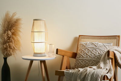 Moderne houten tafellamp met warm licht op witte bijzettafel naast fauteuil met gebreide deken