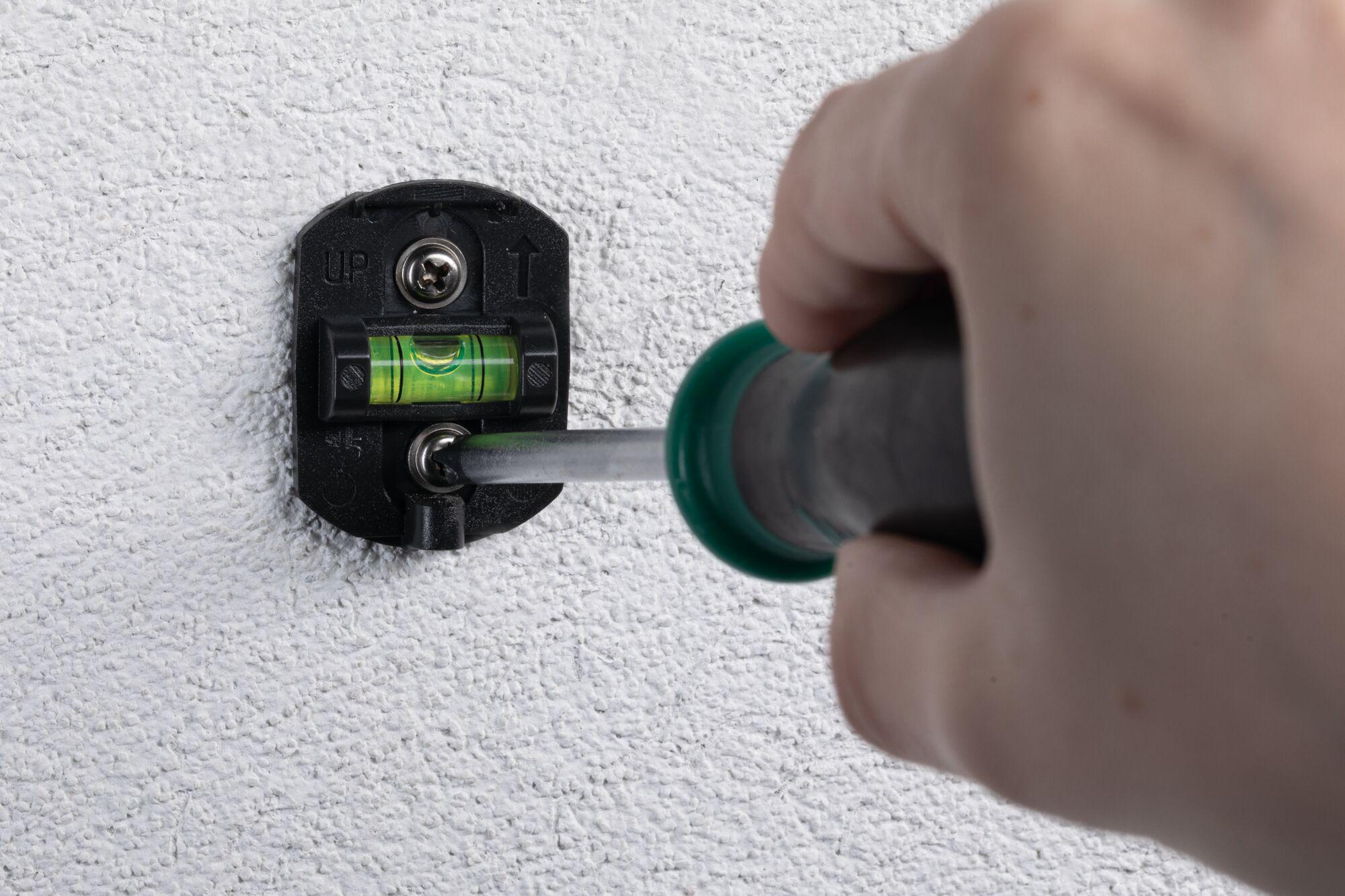 Black plastic wall mount with spirit level being fixed with screwdriver on white textured wall