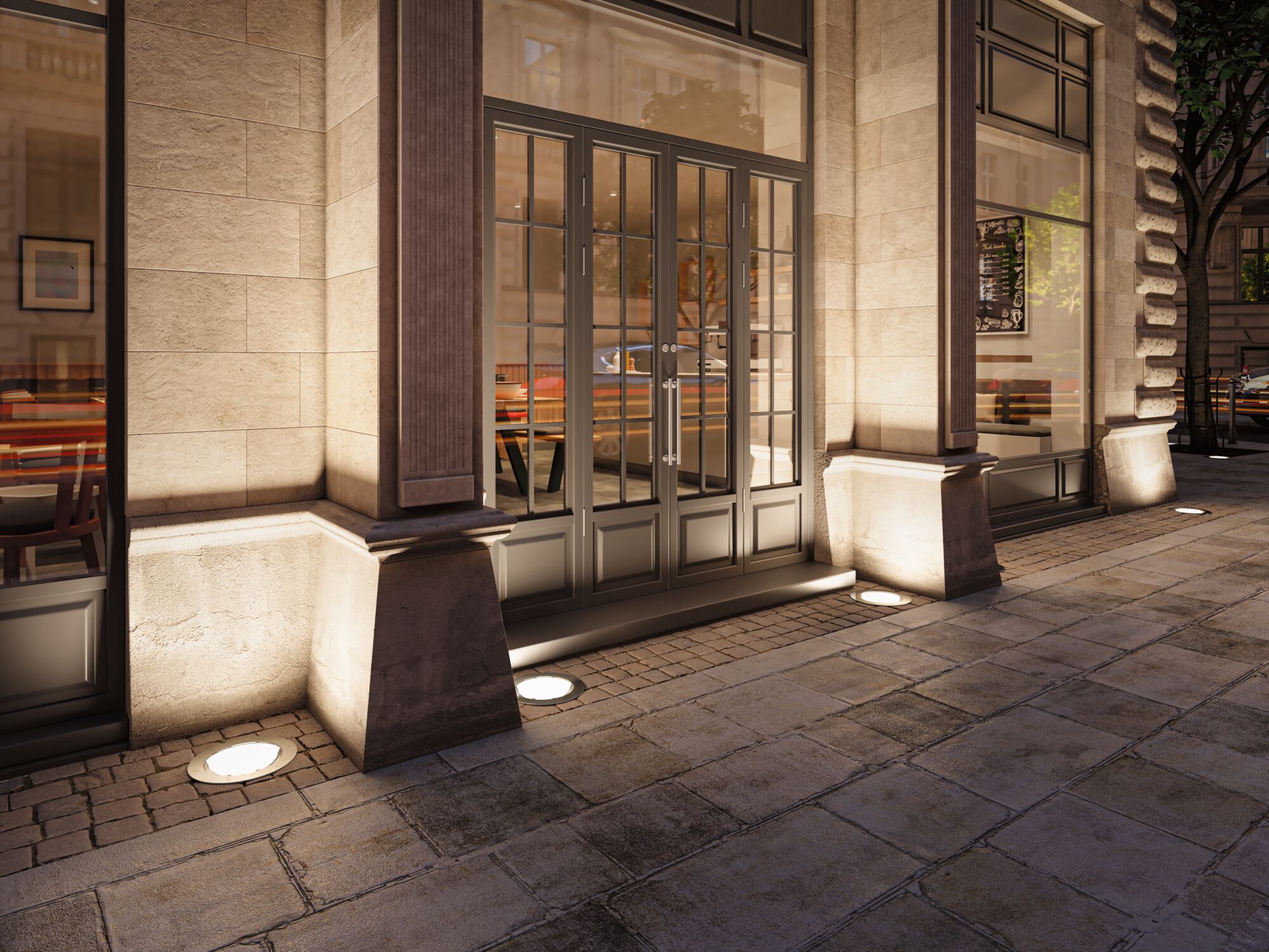 Outdoor round stainless steel recessed floor lights illuminating a sandstone building facade.