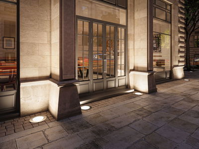 Outdoor round stainless steel recessed floor lights illuminating a sandstone building facade.