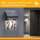 Solar-powered house number light with integrated twilight sensor covered in snow on grey wall