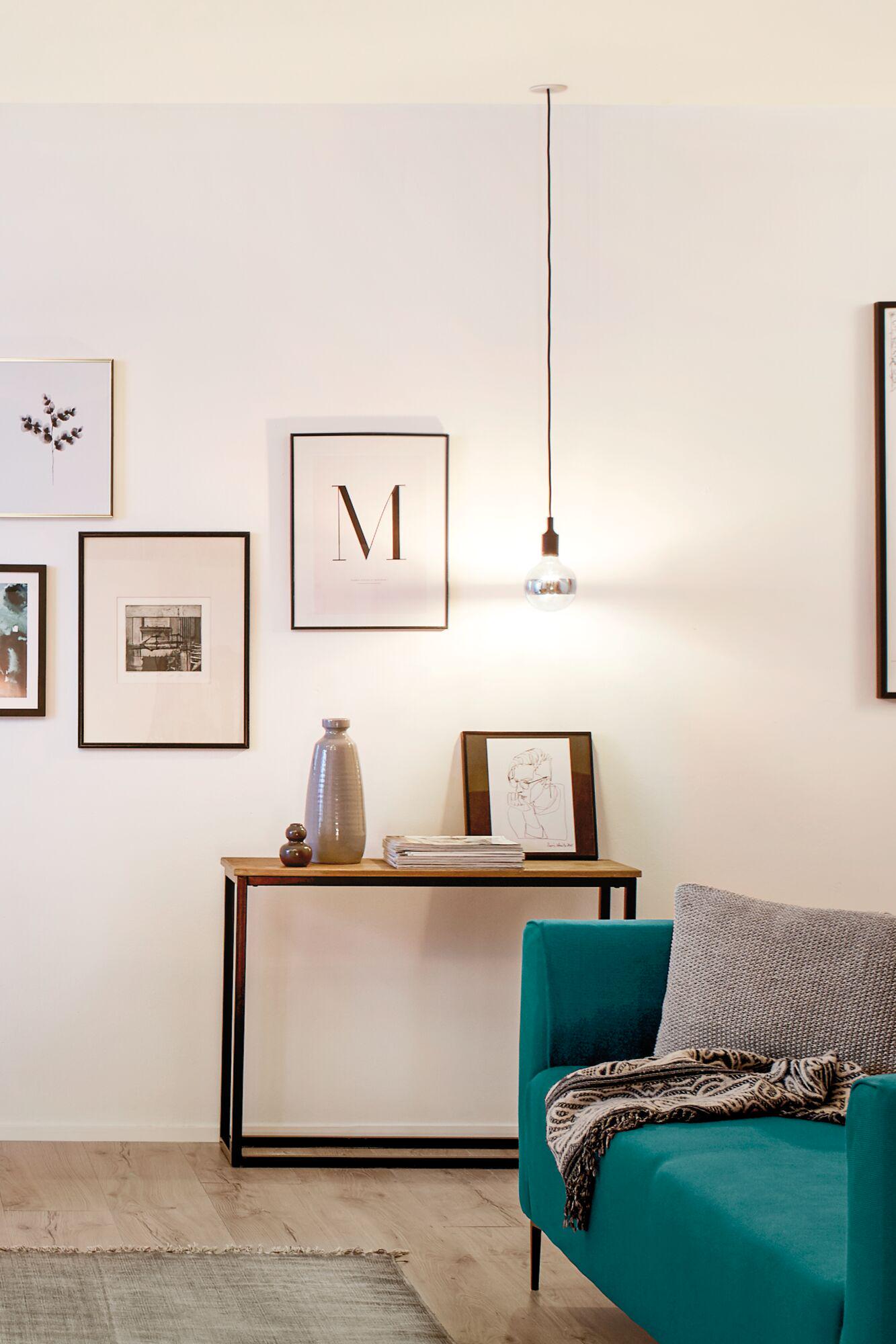 Minimalist pendant light with black cord and clear bulb in modern living room with teal sofa and wall art.