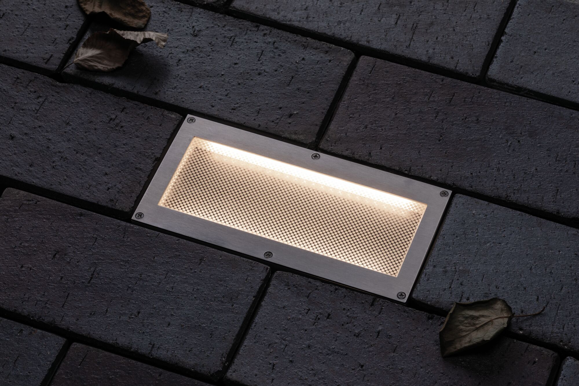 Rechteckige Edelstahl-Einbauleuchte mit warmweißem Licht in dunklem Pflasterboden für Außenbereiche