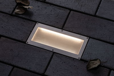 Rechteckige Edelstahl-Einbauleuchte mit warmweißem Licht in dunklem Pflasterboden für Außenbereiche