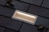 Rectangular stainless steel recessed light with warm white glow in dark outdoor paving for garden lighting