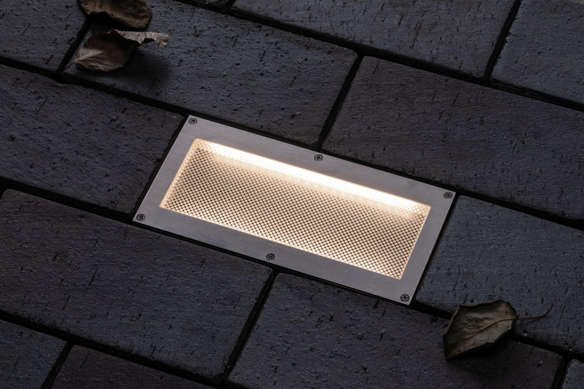 Rectangular stainless steel recessed LED light with warm white glow in dark outdoor paving stones