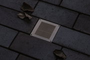 Square stainless steel floor light with mesh insert on dark paving stones with autumn leaves