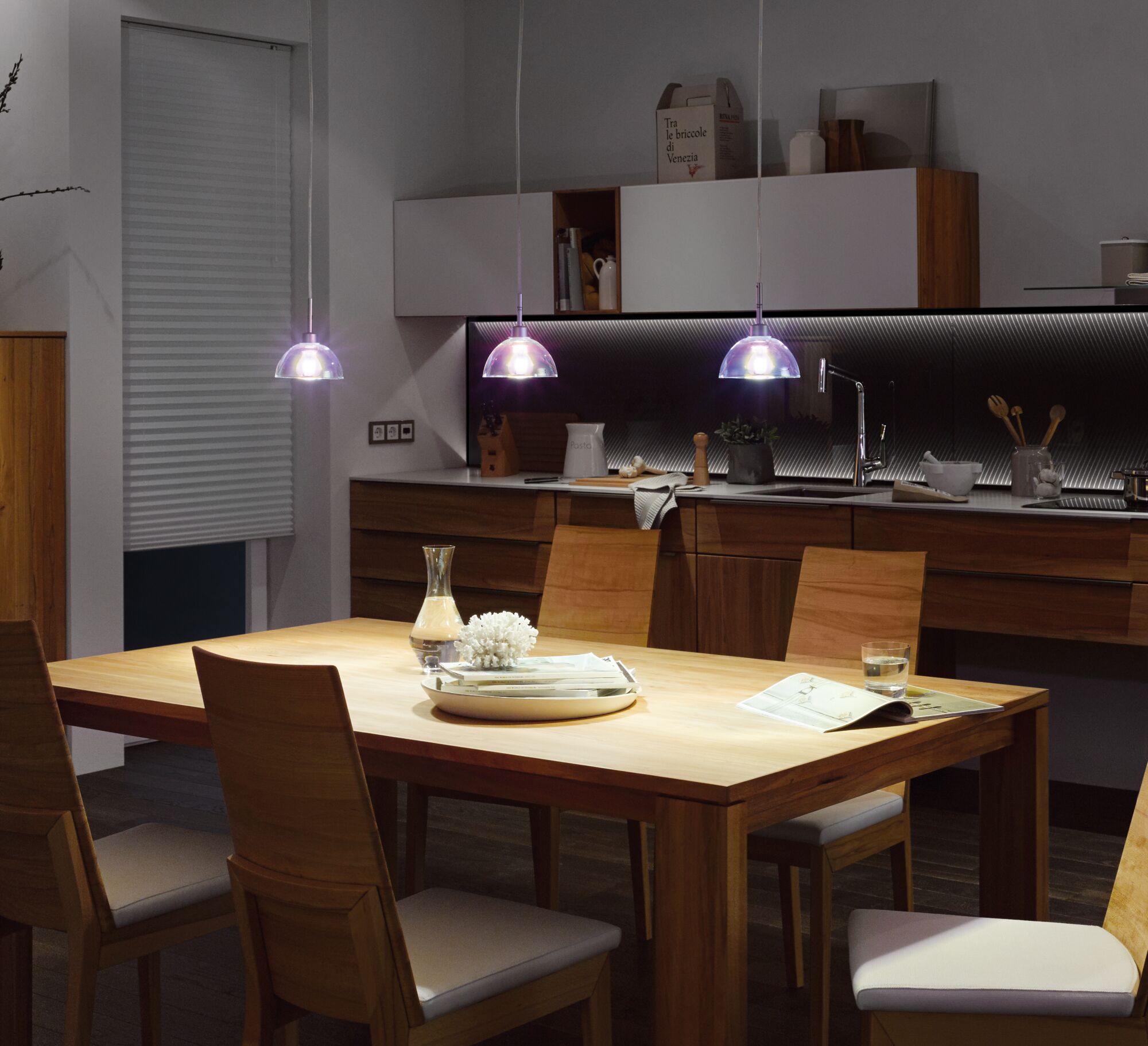 Cuisine moderne avec table à manger en bois et trois suspensions transparentes à éclairage LED.