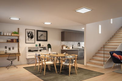 Modernes Esszimmer mit Holzstühlen, Teppich und minimalistischer LED-Deckenbeleuchtung in warmweiß.