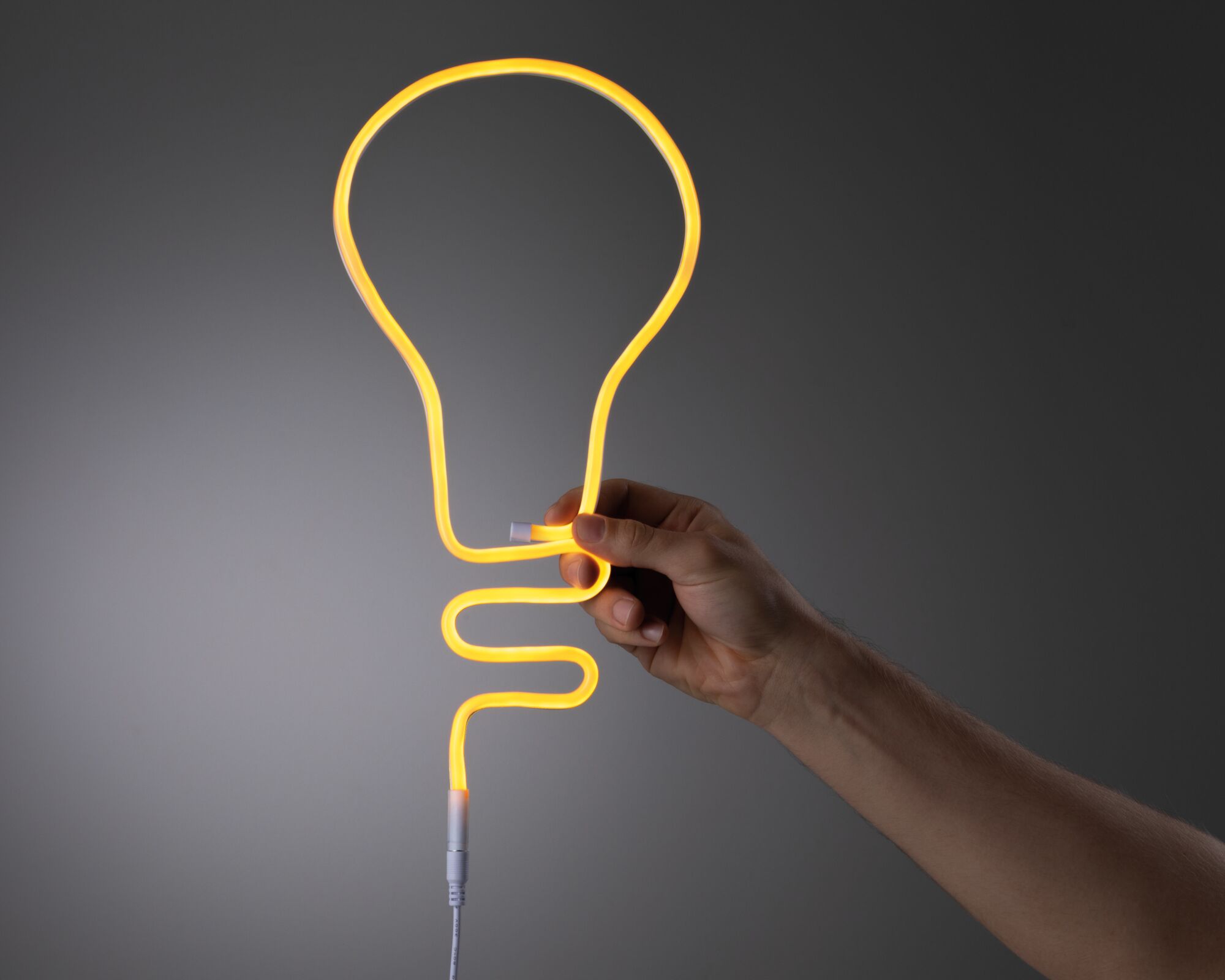 Hand holding flexible yellow neon light shaped like a bulb made of plastic for decorative LED lighting