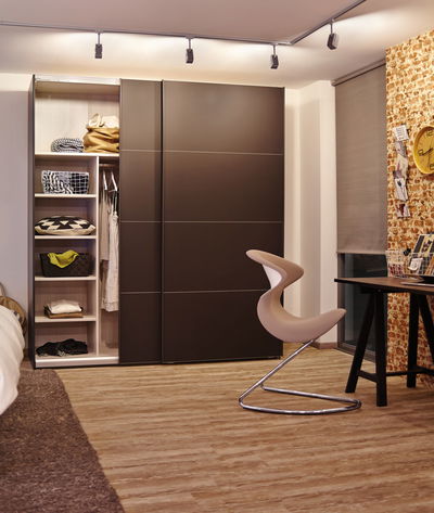 Modern bedroom with brown wooden sliding door wardrobe and beige designer chair with metal frame
