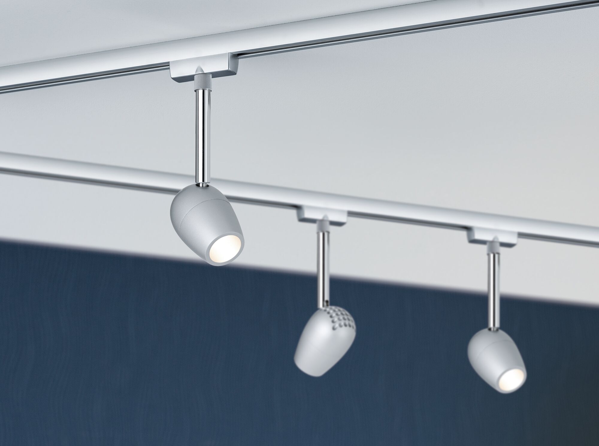 Drei silberne LED-Strahler aus Metall an Schienensystem vor dunkelblauer Wand für moderne Raumbeleuchtung