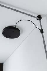 Sort rund loftbeslag med gråt tekstilkabel og klemme på hvidt loft til moderne belysning